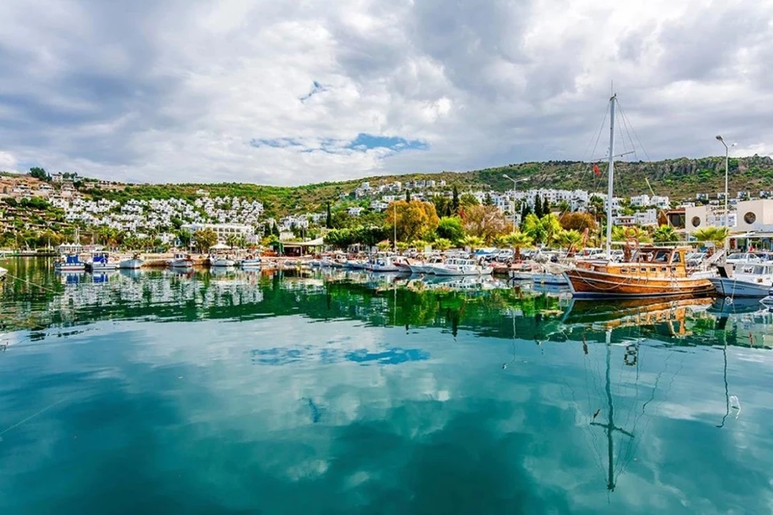 Gümüşlük Bodrum fishing village with turquoise water, traditional boats, waterfront restaurants where guests dine with feet in Aegean Sea at sunset
